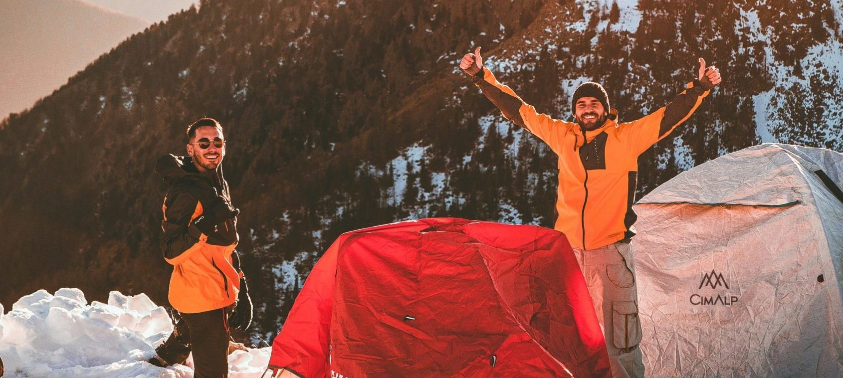 deux hommes souriants se tenant près d'une tente dans la montagne